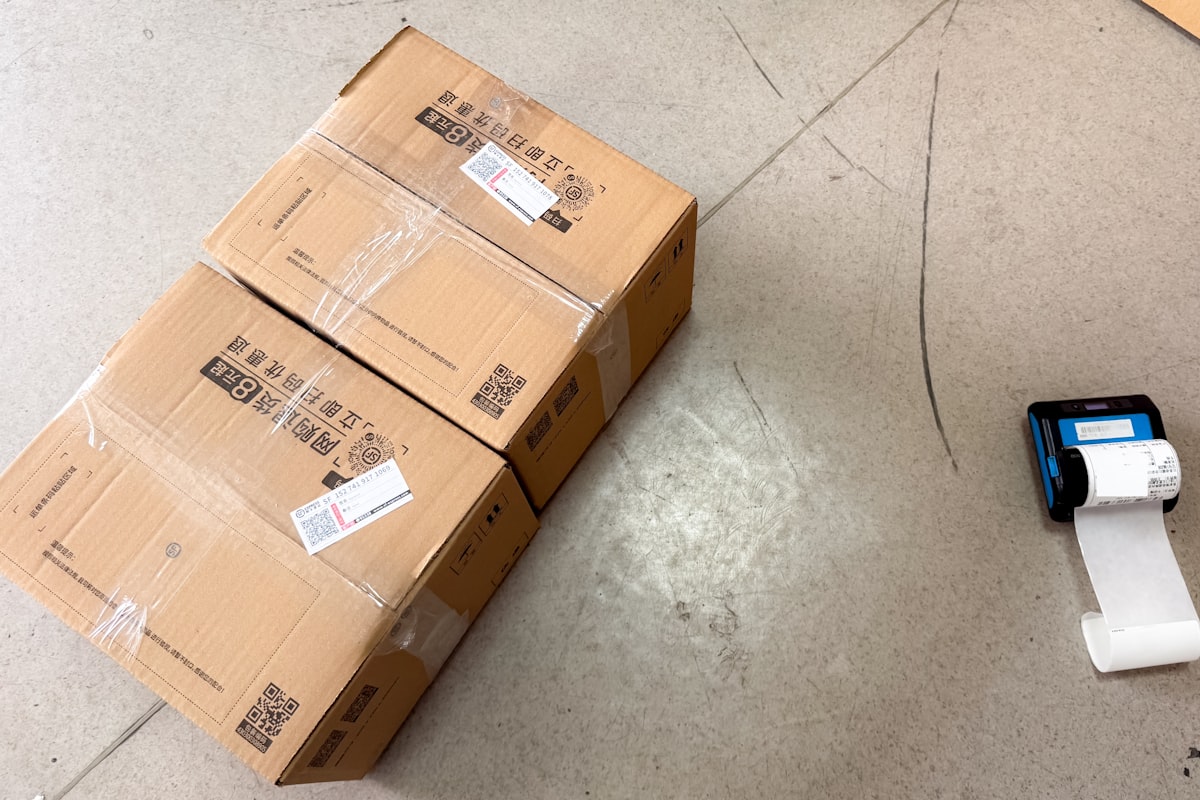 A thermal label printer feeding a freshly printed barcode label beside labeled shipping cartons