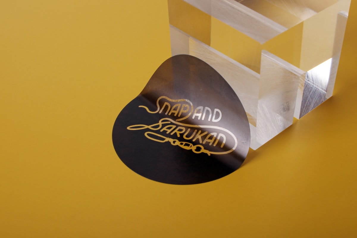 A high-gloss black die-cut label with gold lettering catching a bright specular sheen
