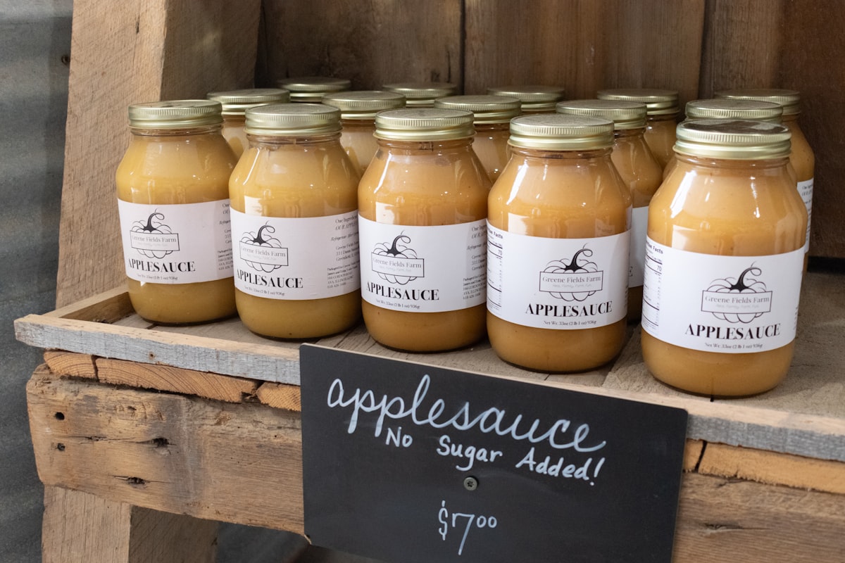 Glass jars of applesauce on a wooden crate, each with a printed front label and nutrition-facts panel