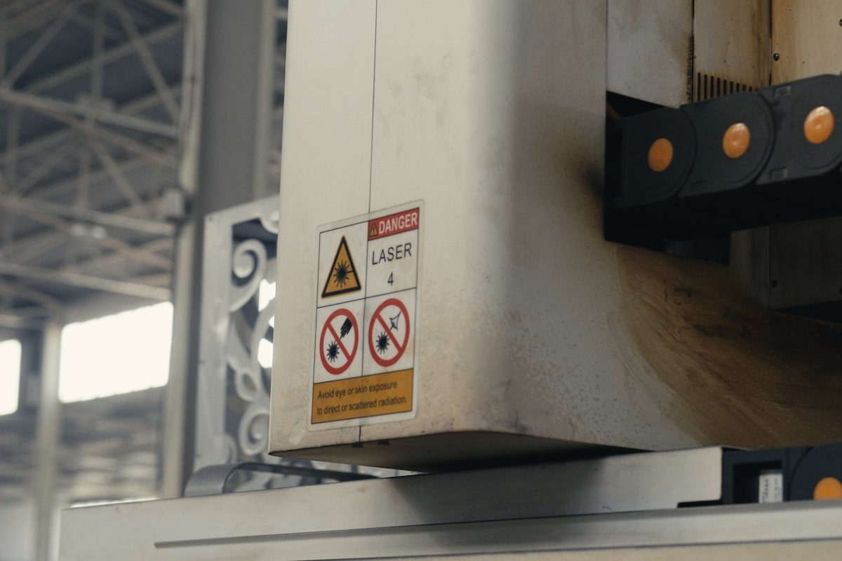 A printed adhesive safety label applied to industrial laser-cutting equipment on a factory floor