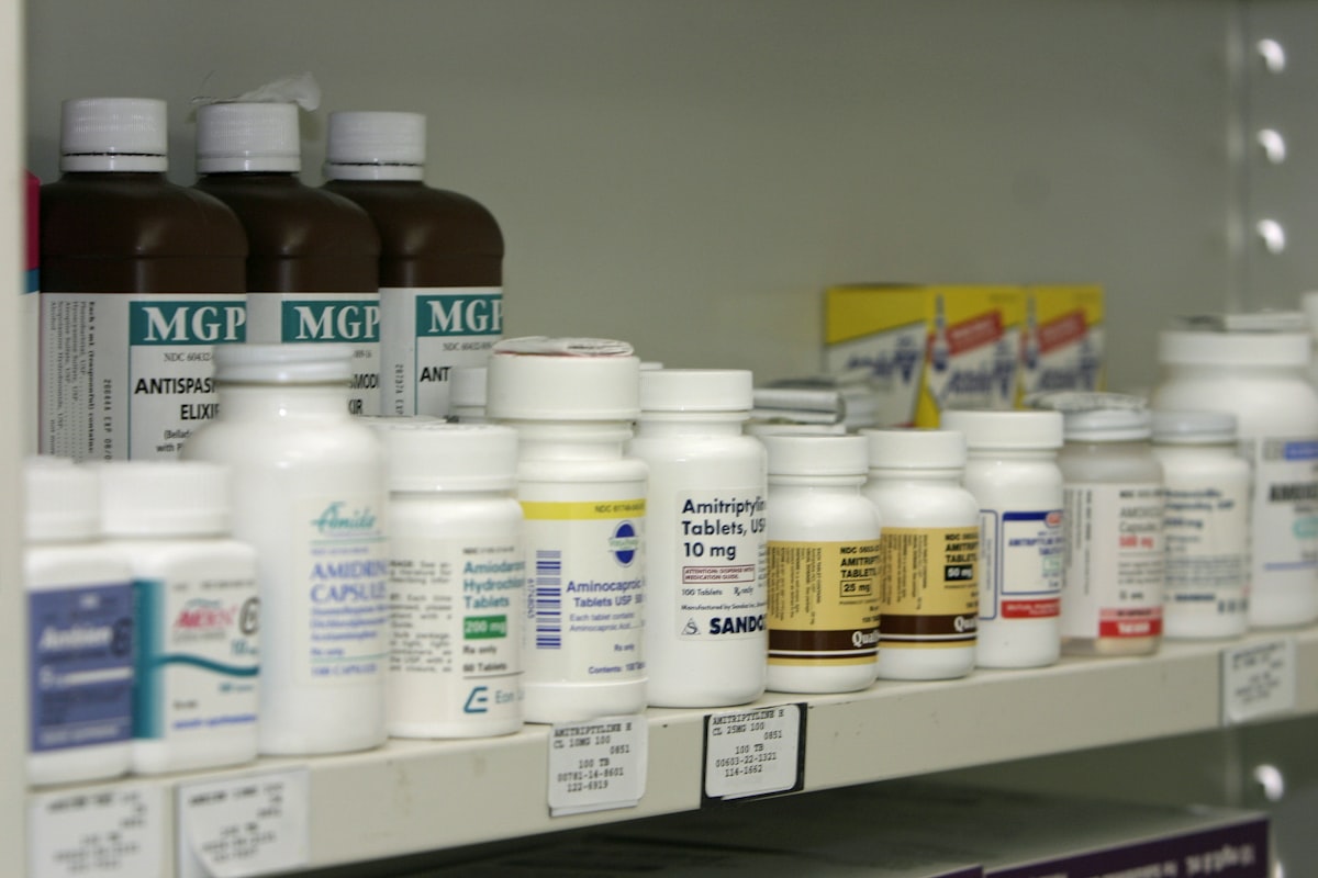 Pharmacy shelf of labelled medicine bottles with drug codes, alongside barcoded bin labels